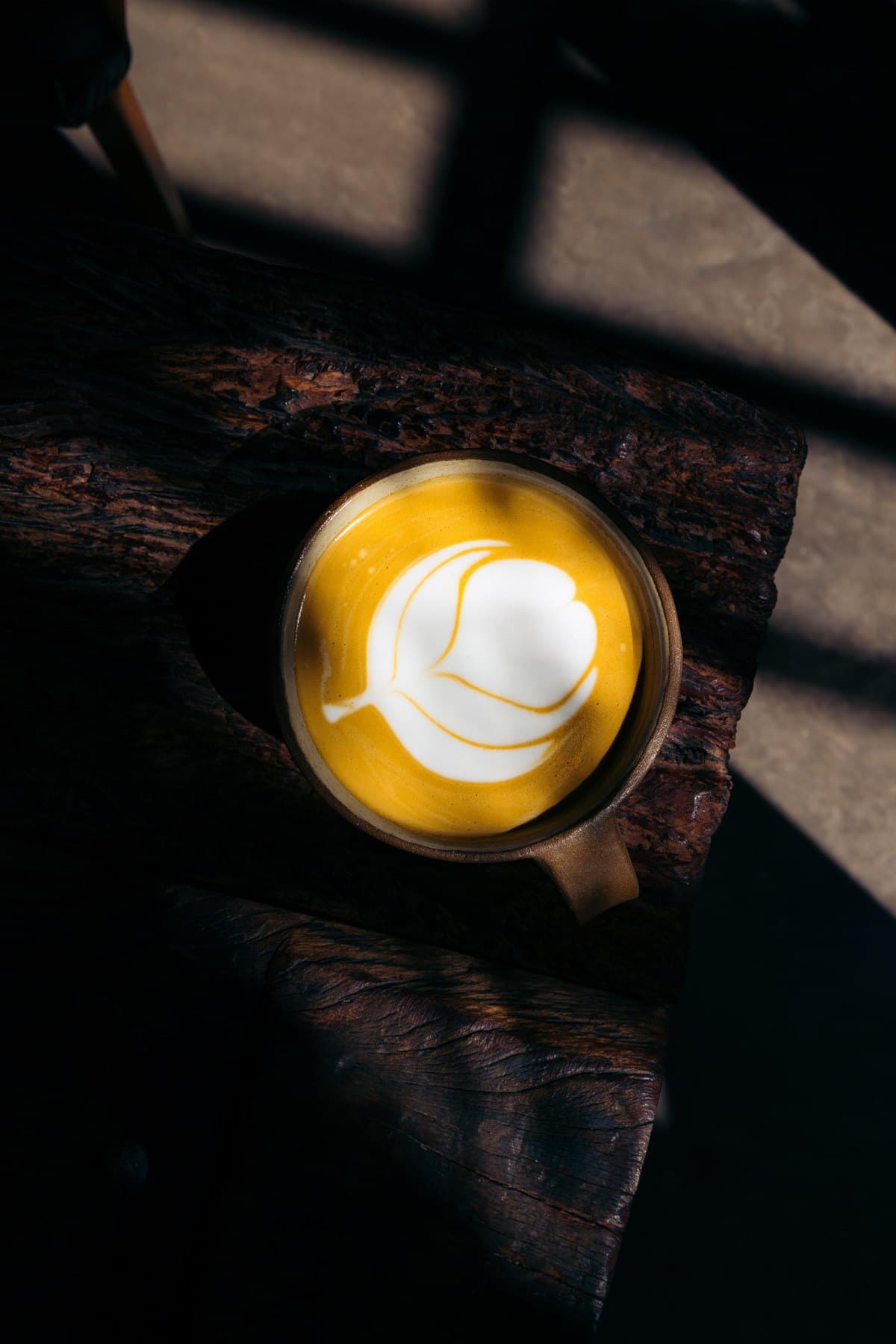 Café con leche con latte art sobre una mesa de madera, al sol